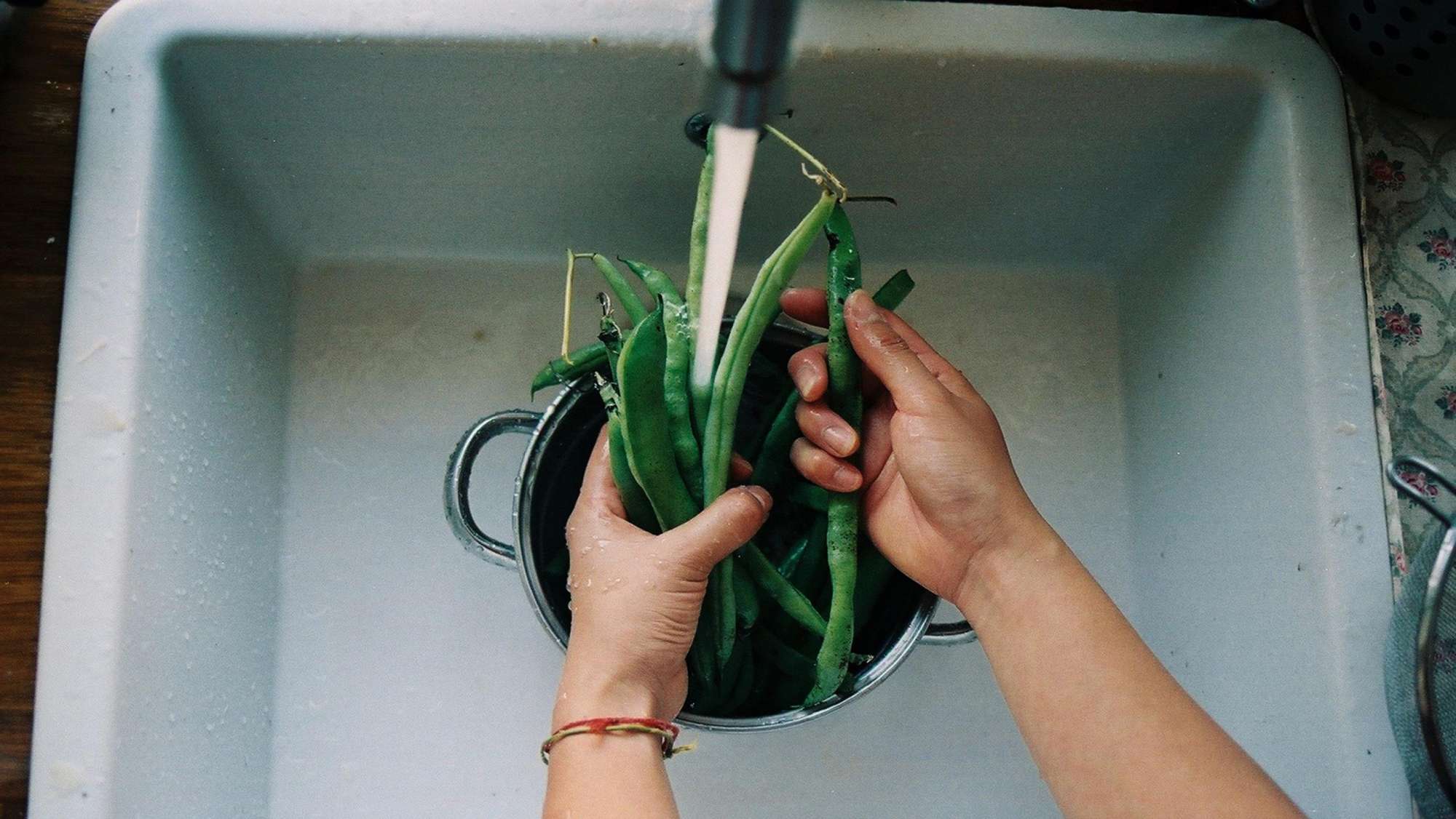 Hände waschen grüne Bohnen in einem Waschbecken als Symbol für Ernährungstipps bei Krebs.