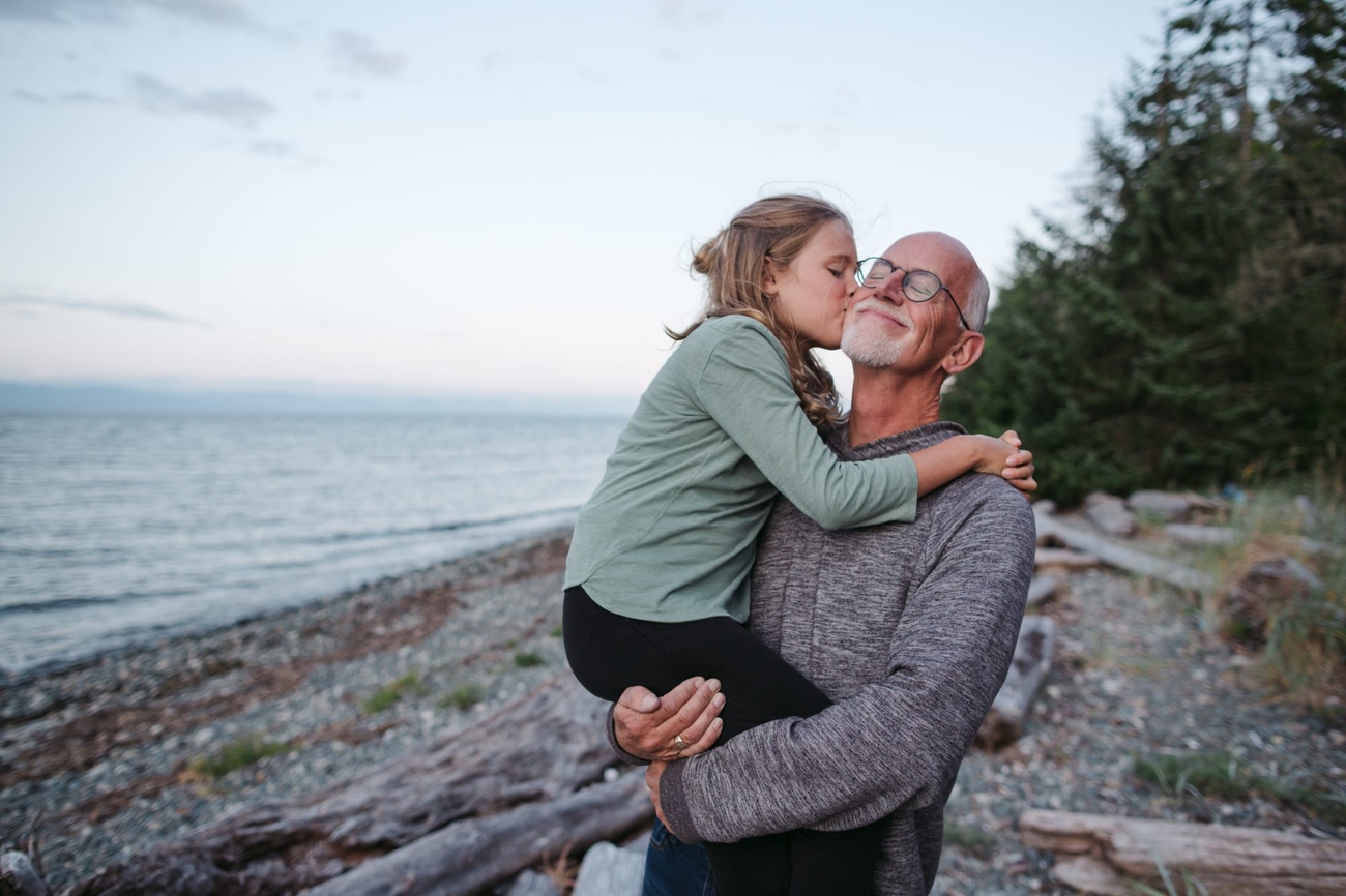 Au bord de l’eau, une jeune fille embrasse son grand-père sur la joue.