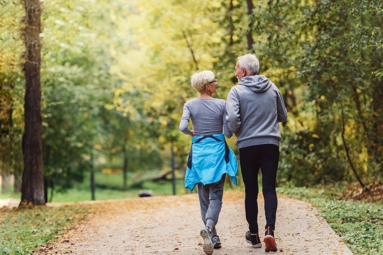 Older couple taking a stroll in autumn while wearing matching gray sweaters.