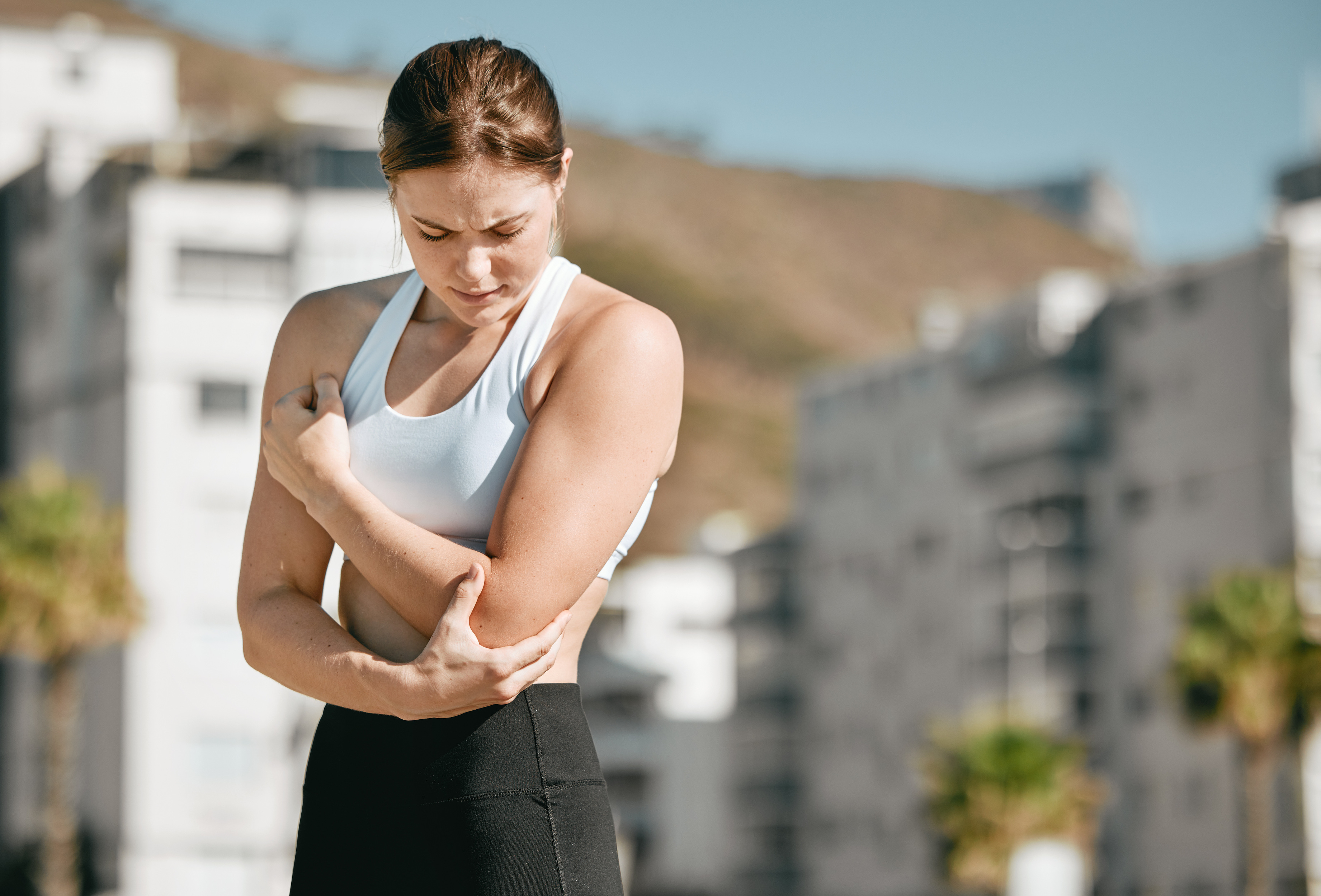 A woman in athletic wear, holding her arm in discomfort.