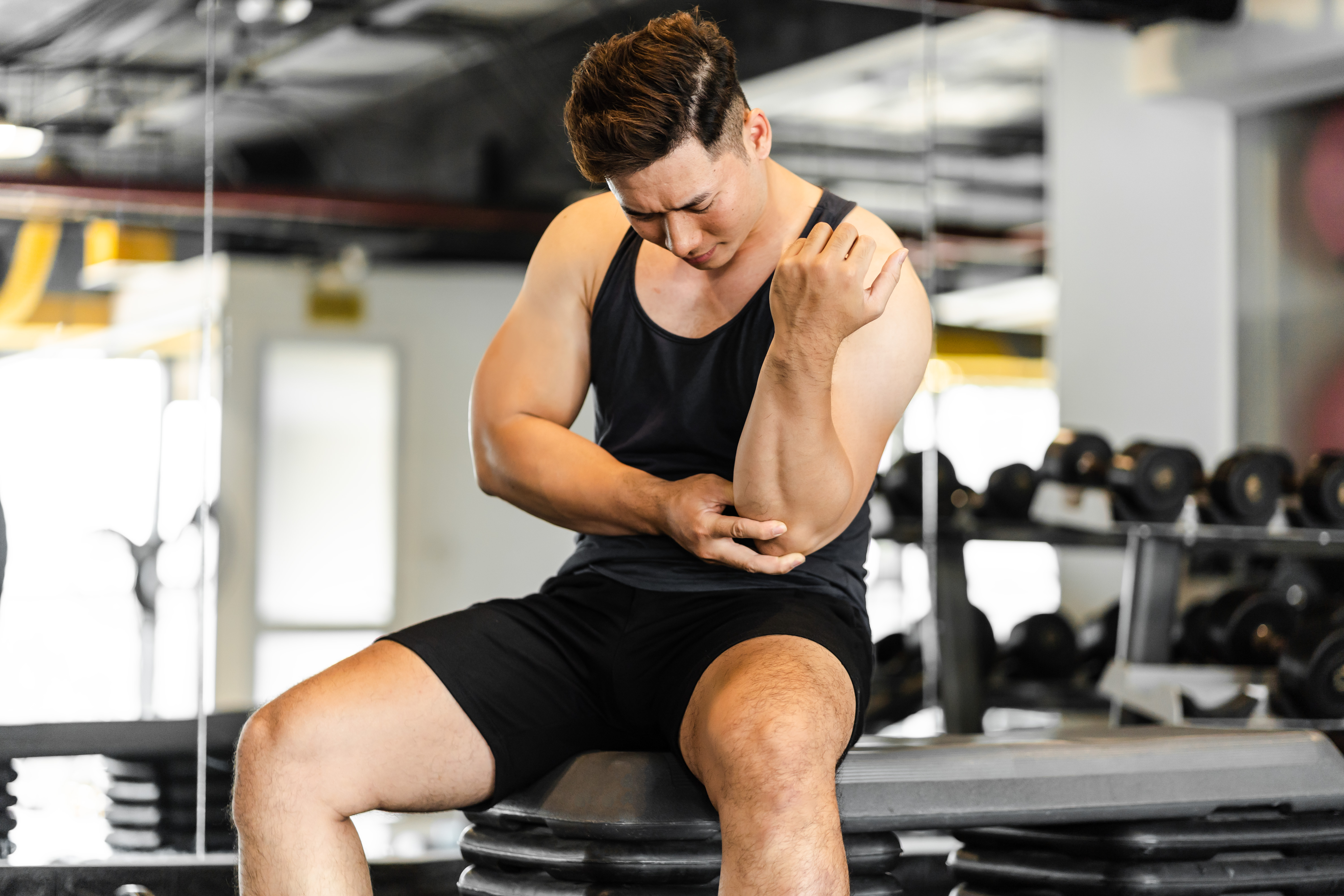 man feeling pain in elbow while sitting inside gym