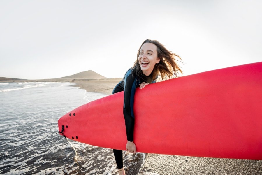 Woman holding red surfboard on sandy beach.