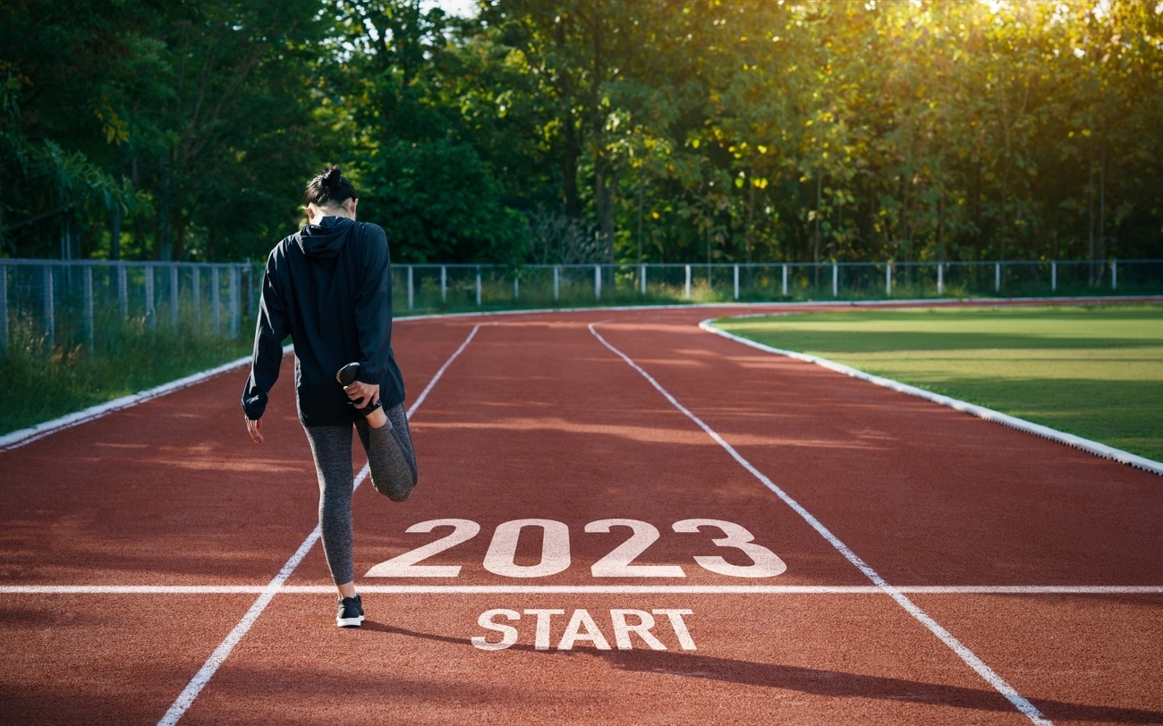 A female athlete running on a track with 2023 start in the background.