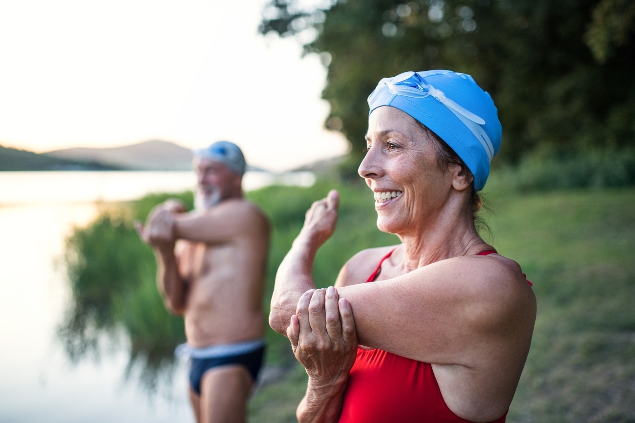 Deux nageurs portant un bonnet de natation s’étirent les bras en souriant avant de plonger à l’eau.