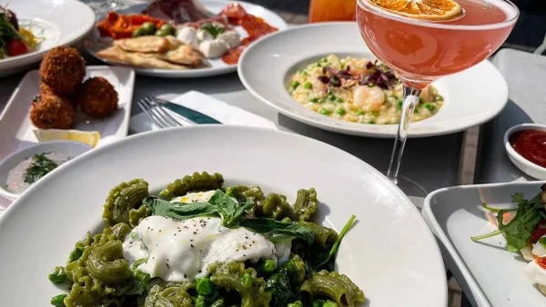 A generous serving of spinach creste di gallo with pesto, peas and burrata, with a pink cocktail.  