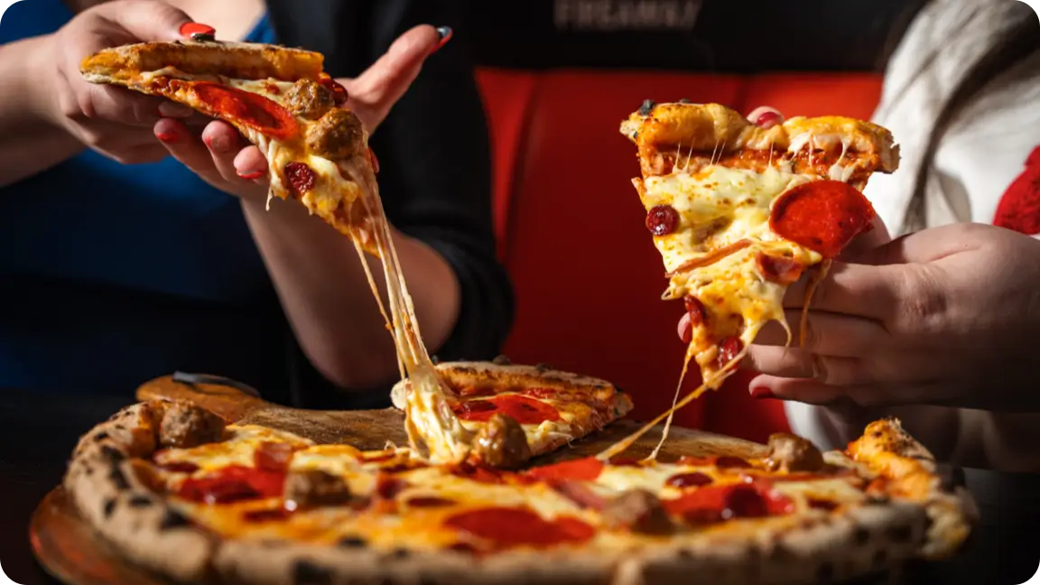 Two people enjoying a cheesy pizza, with lots of cheese being pulled