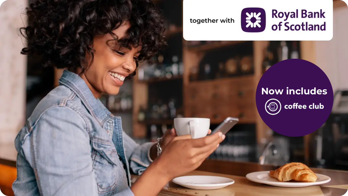 Woman smiling whilst holding her phone and drinking coffee.