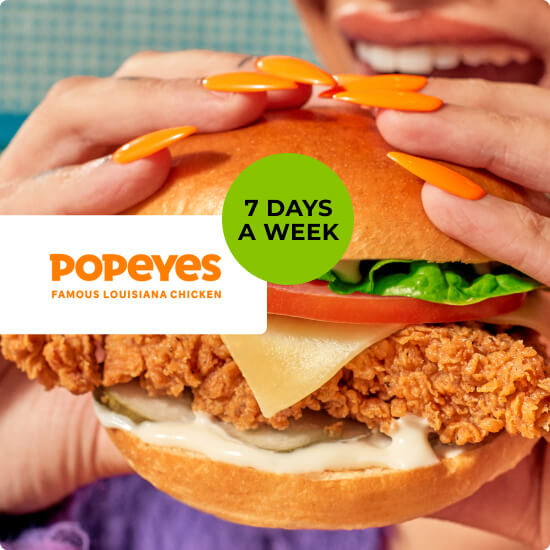 Someone enjoying a bite out of a Popeyes Louisiana Chicken burger, filled with cheese, tomatoes, lettuce, mayo and pickles.