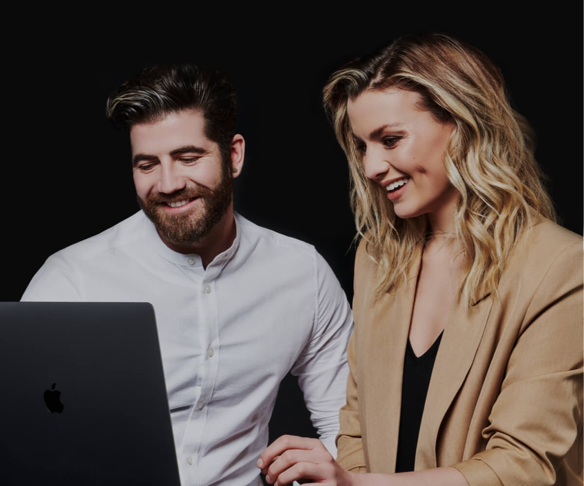 A man and a woman discussing content whilst looking at a laptop screen