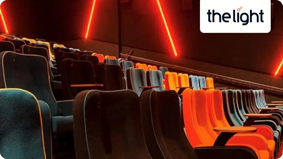 An empty cinema auditorium with colourful tiered seating and red neon lights, featuring The Light logo.