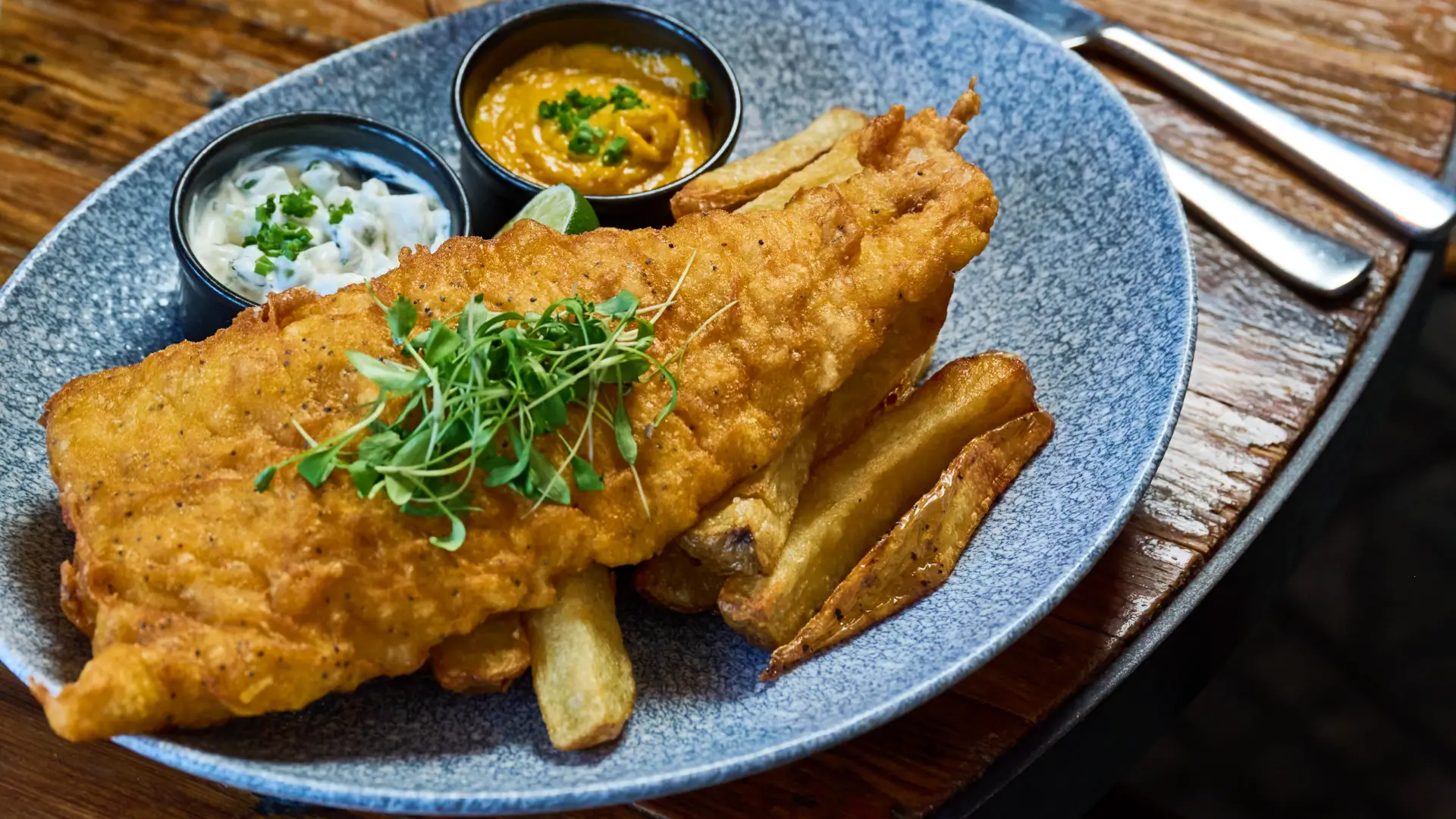 fish and chips with tartare and curry sauce on a blue plate