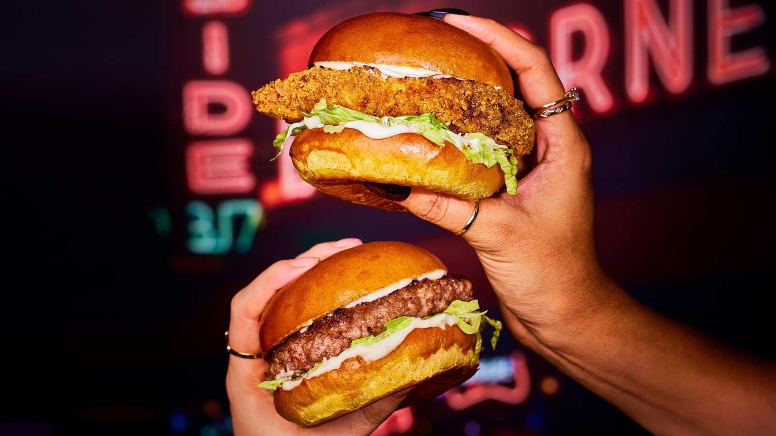 Hands holding two Frankie and Benny's burgers with patties, sauce and salad
