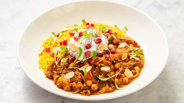 A white bowl filled with jackfruit tagine, topped with pumpkin seeds and pomegranate seeds. 