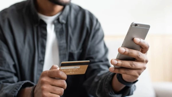 Man holding credit card and using smartphone at home