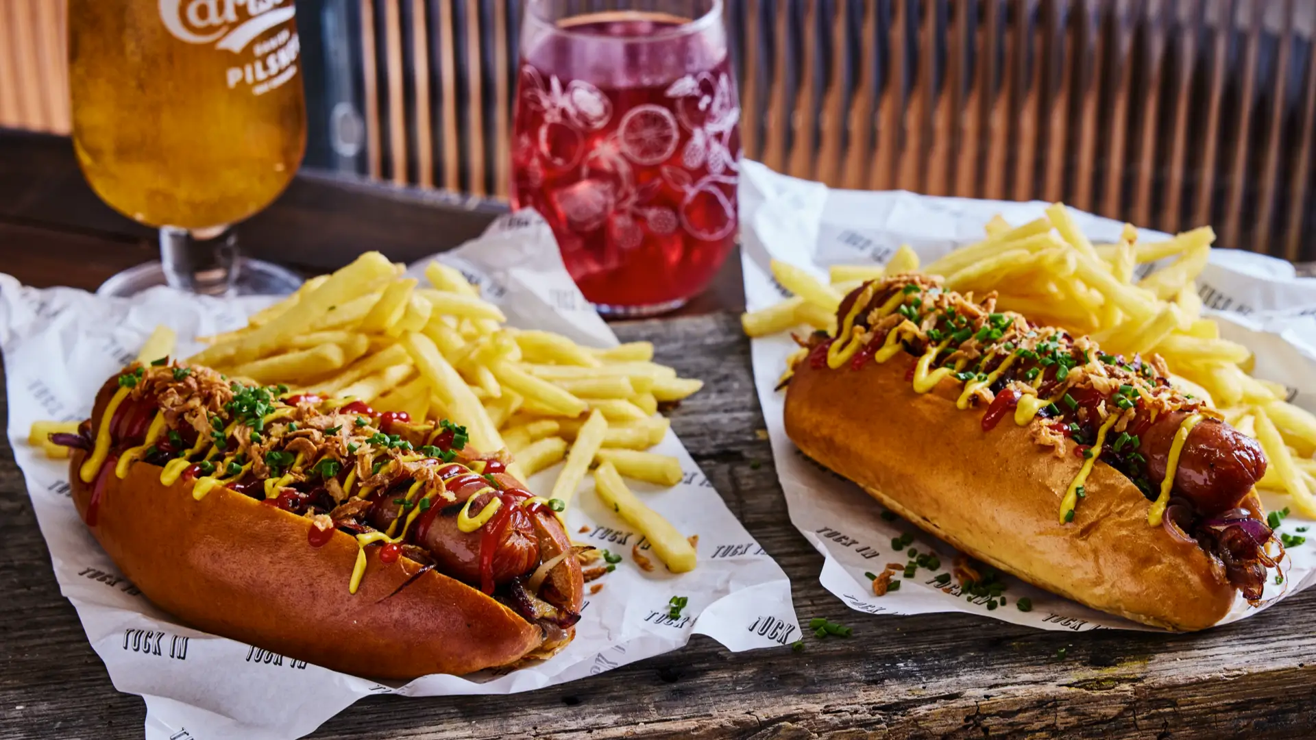 two hot dogs with ketchup and mustard served with fries and beer