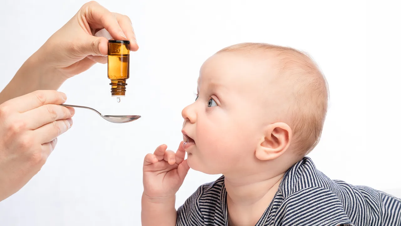 Mother's hand pouring vitamin drops on to spoon for baby boy
