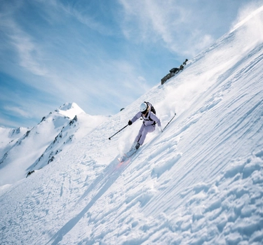 A woman with lila coloured ski jacket from Odlo skiiing on a mountain.