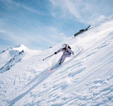 A woman with lila coloured ski jacket from Odlo skiiing on a mountain.