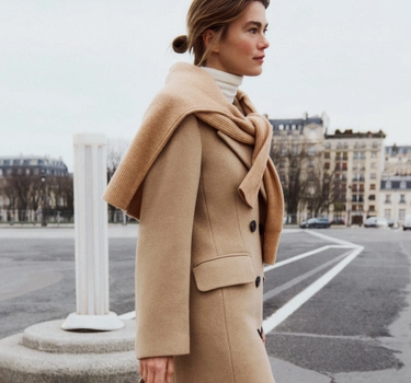 A young woman walking in a city wearing a white sweater, and long brown sleeve jacket for the Fall season from Companys.