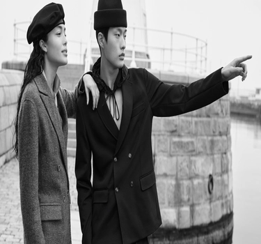 A young woman and an Asian man standing next to a lighthouse with dark-coloured jackets 