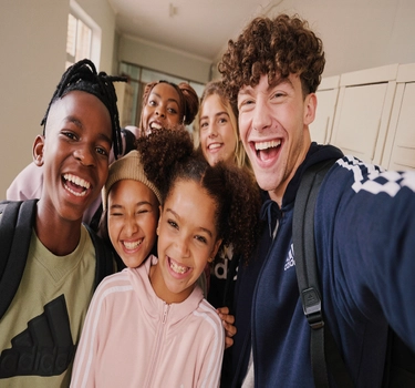 A group picture of children on the hallway of school. All of the children wear several coloured Adidas outfits.