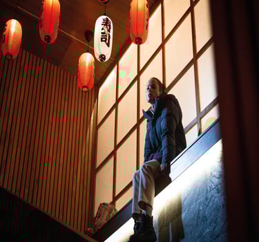 En person sitter på en opphøyd kant i et urbant miljø iført en funksjonell jakke fra SWIMS.