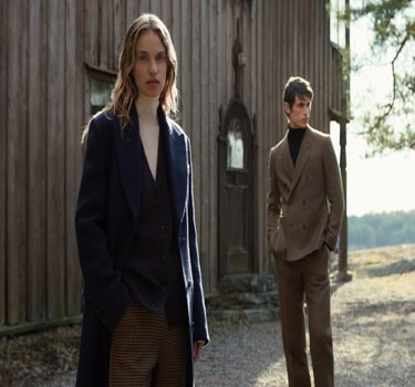 To menn i stilrene kåper og dresser fra Tiger of Sweden foran en rustikk trevegg.