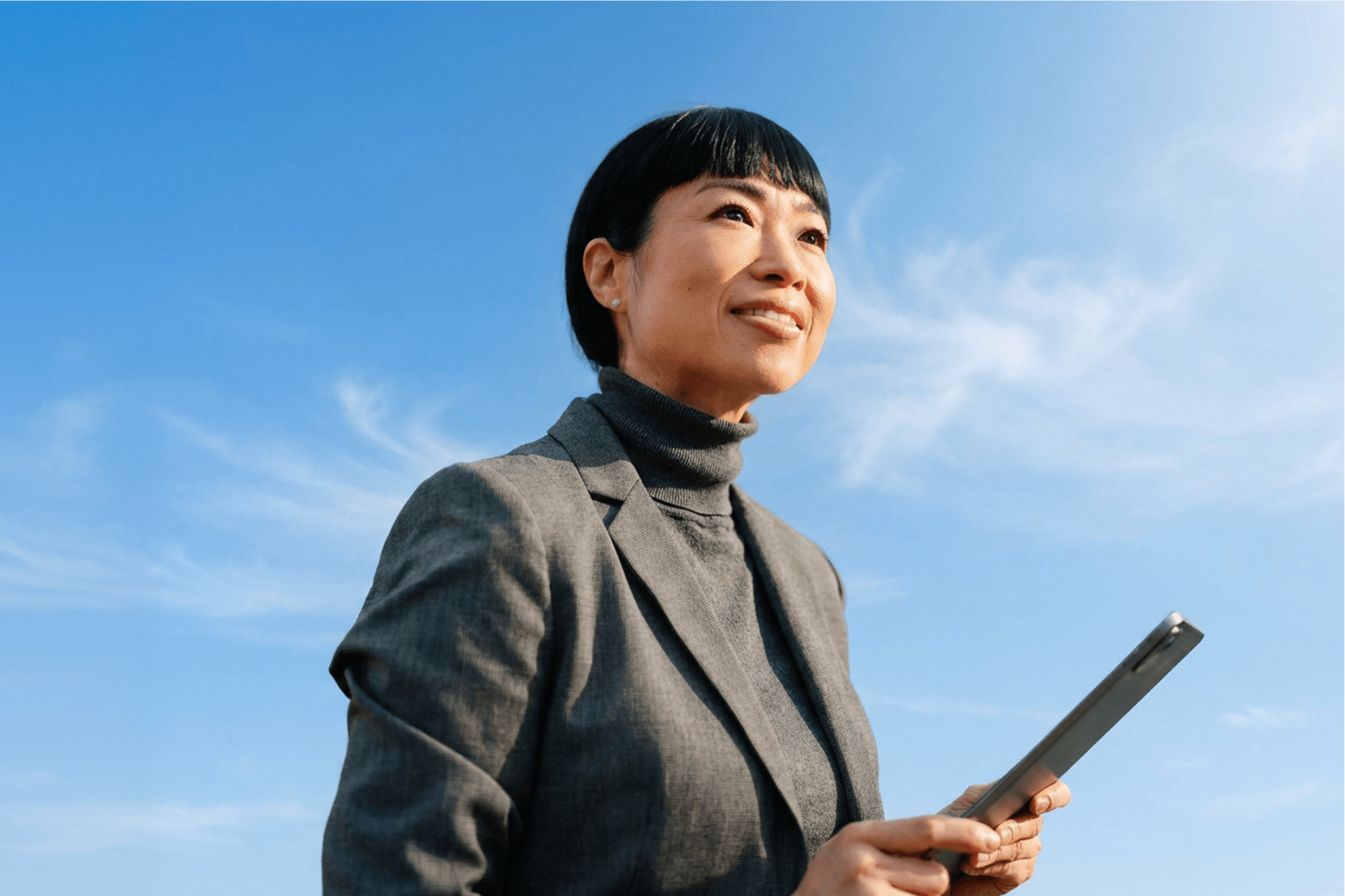 A confident businesswoman looking up against a blue sky