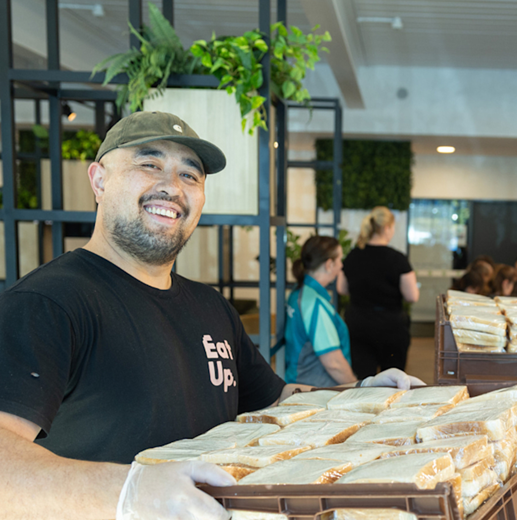 A smiling volunteer holding a tray of sandwiches at a food preparation event