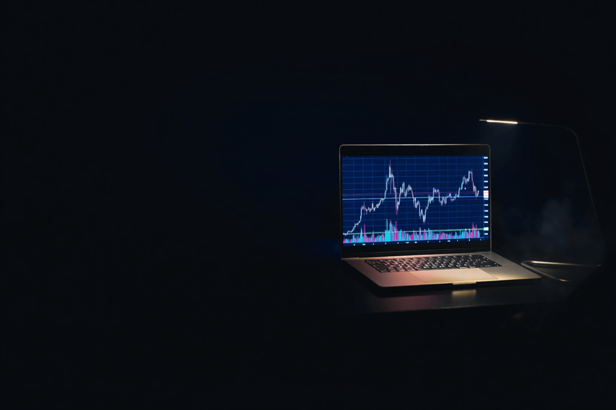A laptop displaying a financial trading chart in a dark room