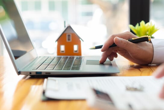 Someone scrolling on their laptop with a pen in their hand