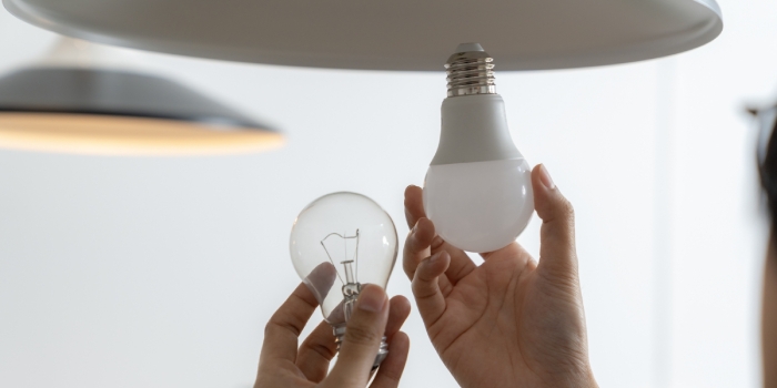 One hand removes a lightbulb, while another raises a new lightbulb towards the connector