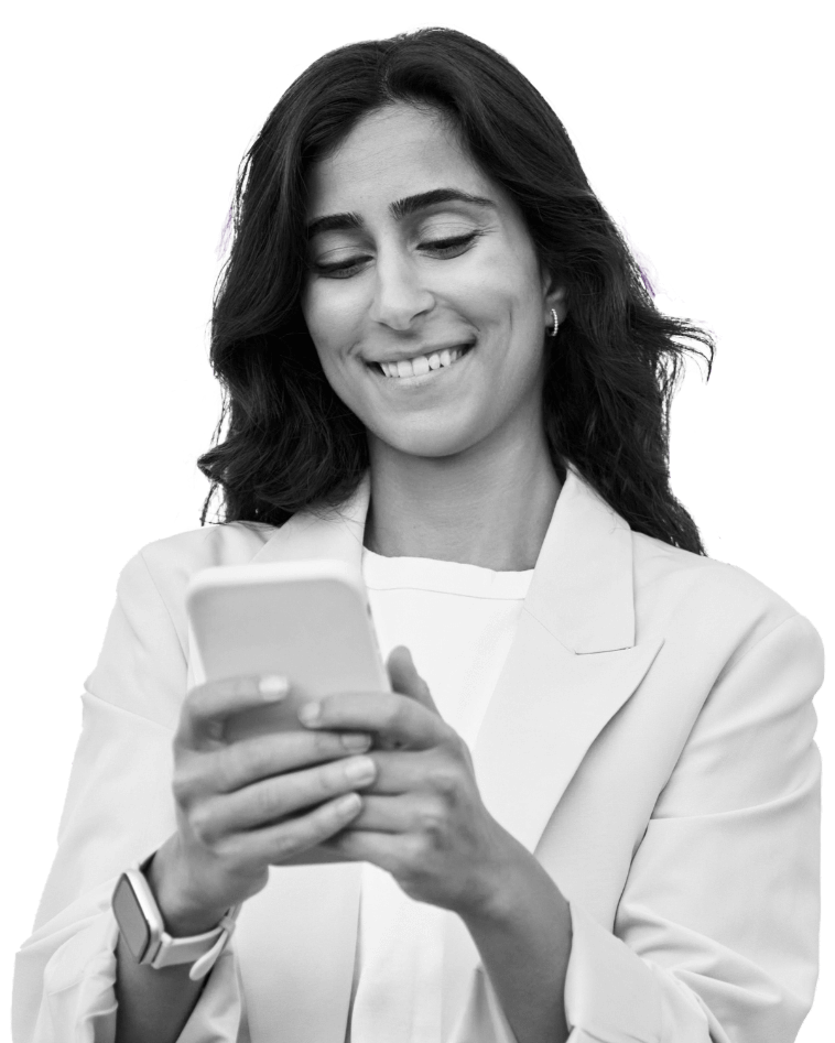 A smiling woman wearing a blazer looking down at the phone in her hands.