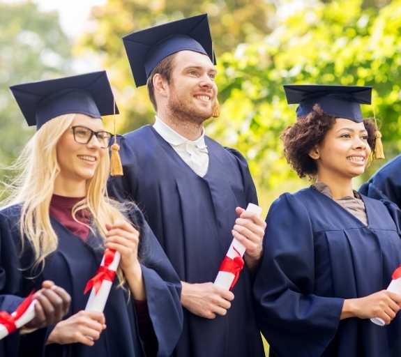 A group of graduates smiling whilst holding their diplomas at their graduation