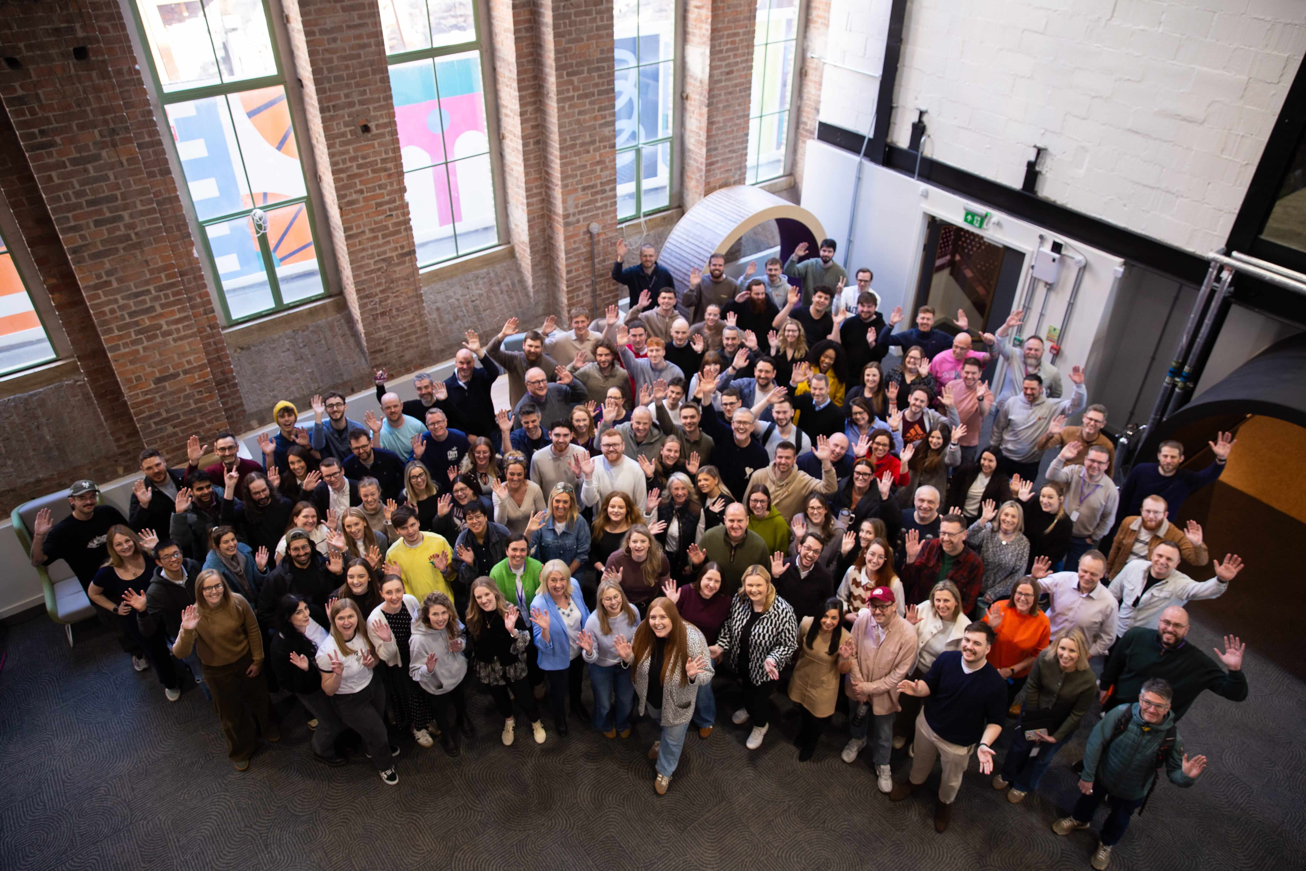 Many Atom bank staff, waving and smiling, in the Atom headquarters at the Pattern Shop