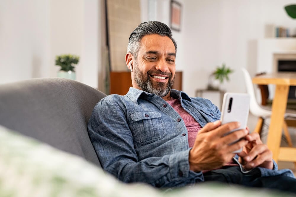 A person slouched on a sofa looking at their phone and smiling