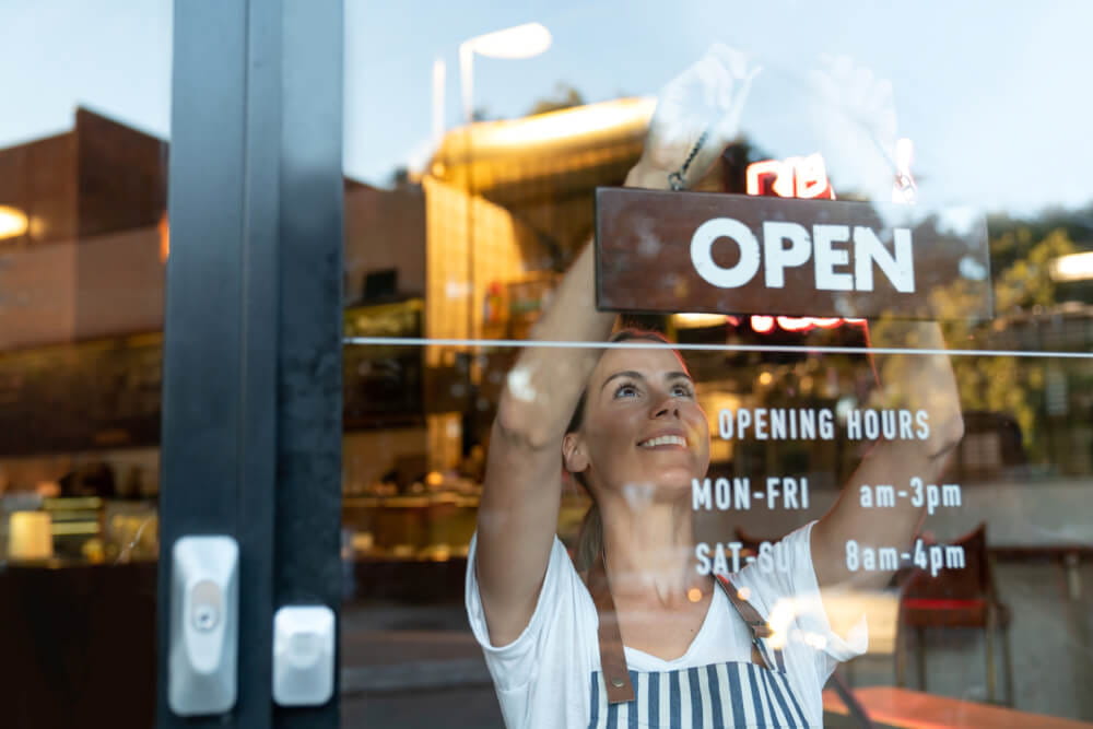 A woman turning a business sign around to display open