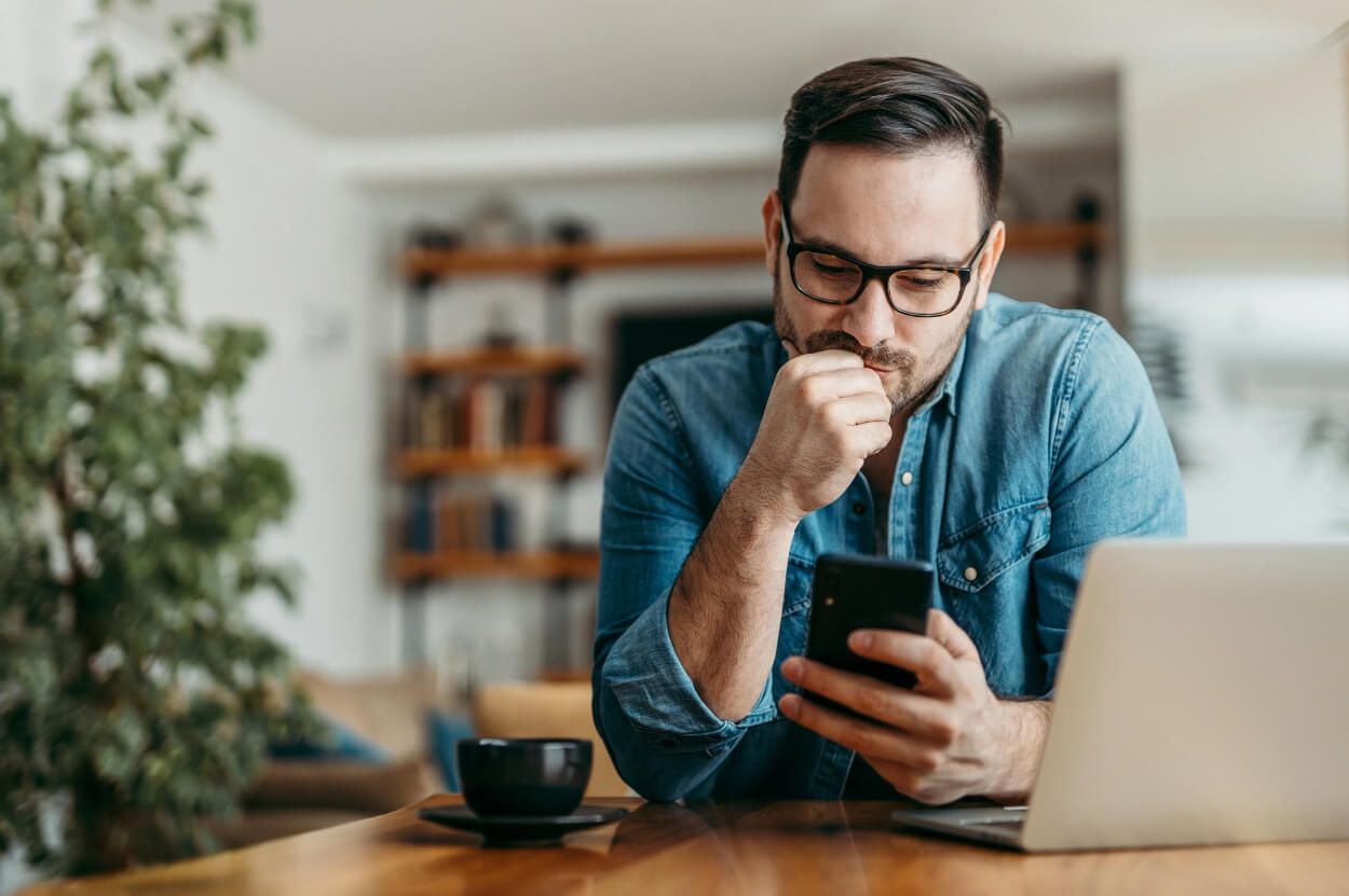 A man wearing a denim jacket sitting at a table on his phone