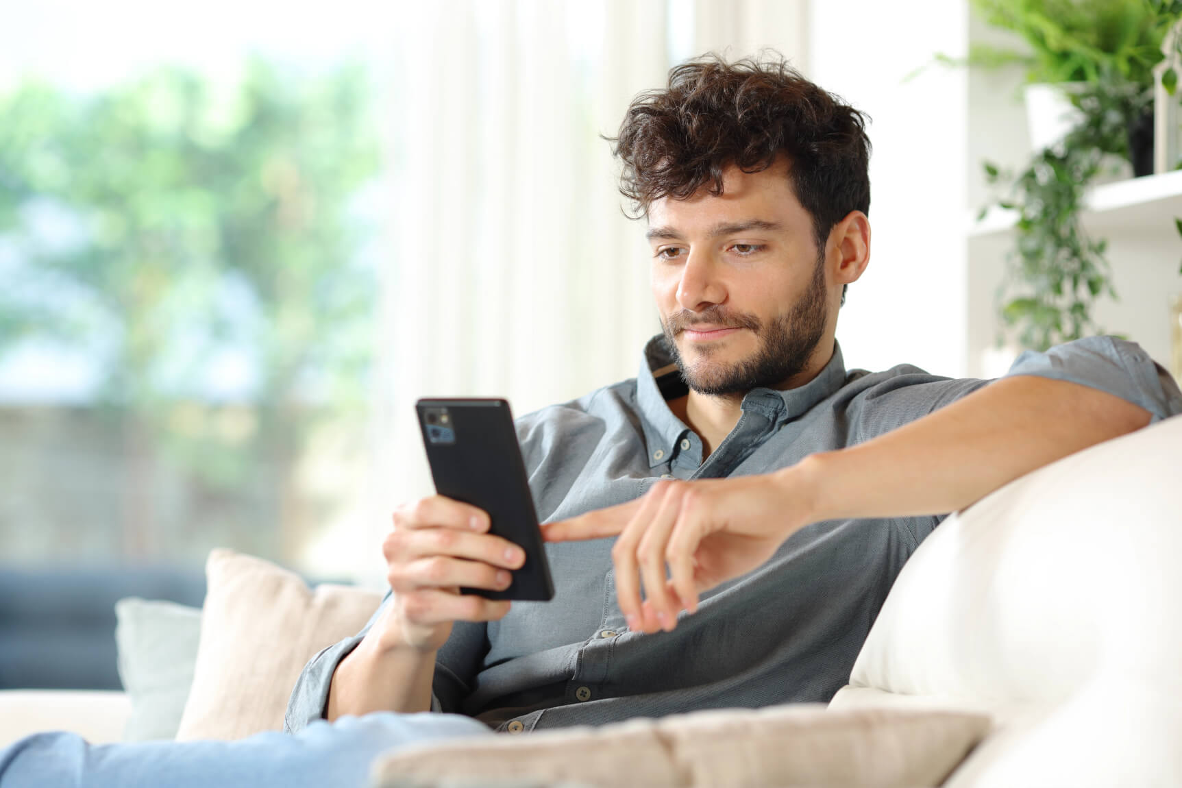 A man sitting on the sofa holding his phone and scrolling