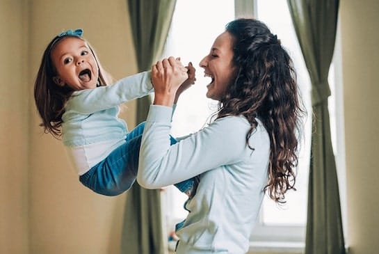 A woman playfully lifting up their child and laughing 