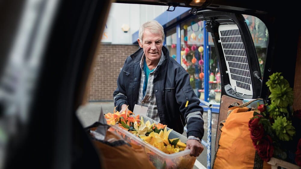 A person moving a box of flowers into the back of a van