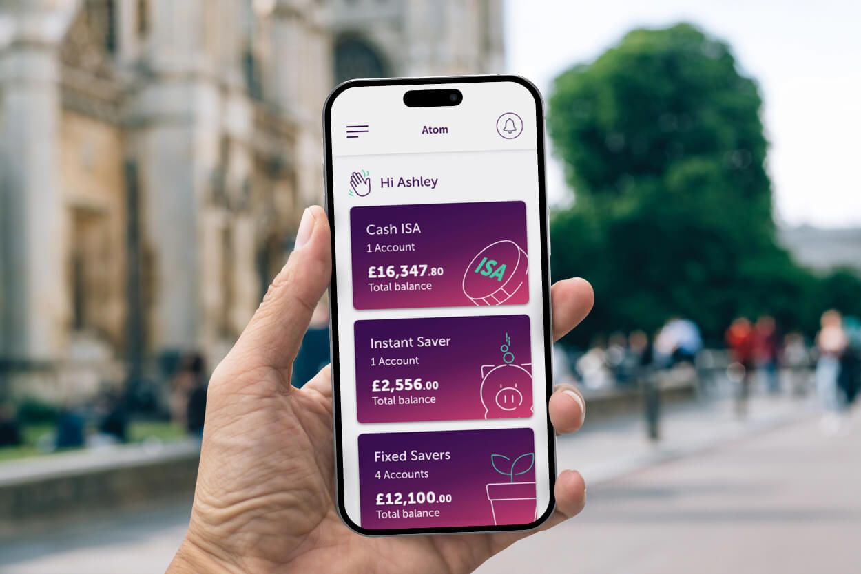 A hand holding a phone with atom bank app homepage on it