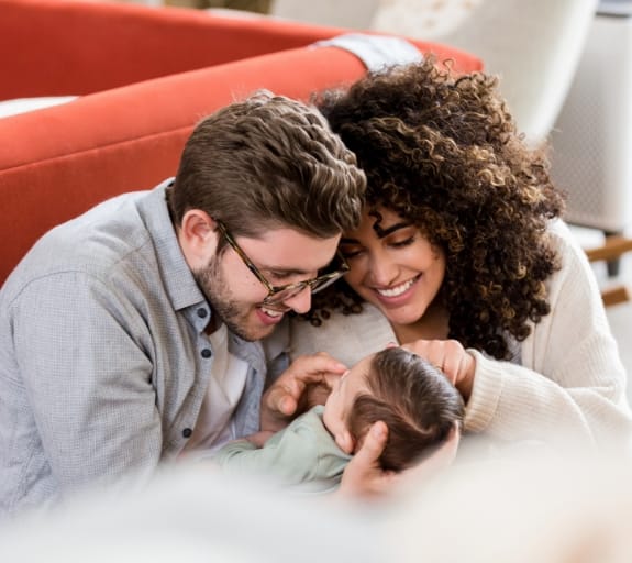 A couple holding their baby whilst cheerfully smiling at them