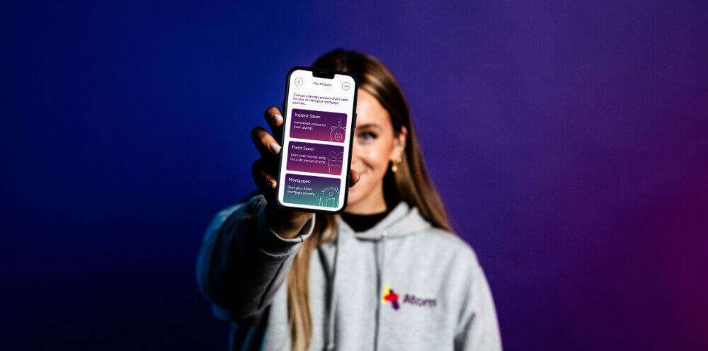 Woman holding a phone out in front displaying the atom bank app products page