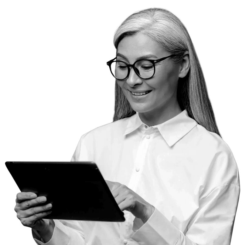 A woman wearing glasses is smiling whilst looking down at her tablet