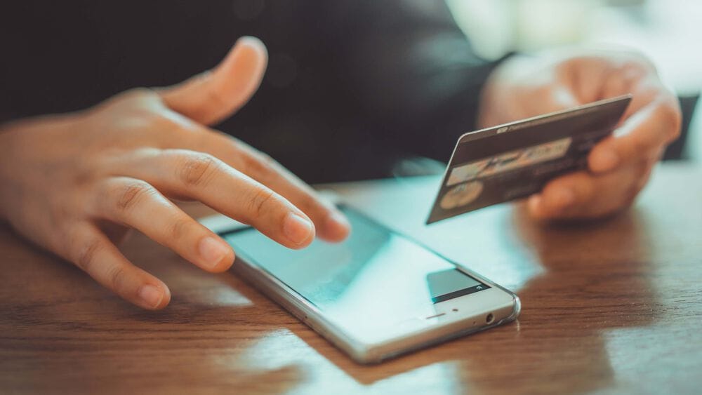 A person holding their credit card and paying for something on their phone