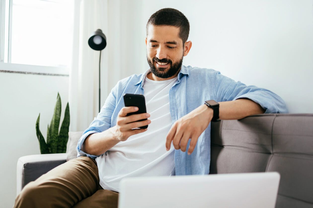 Person sitting on sofa looks at their phone and smiles