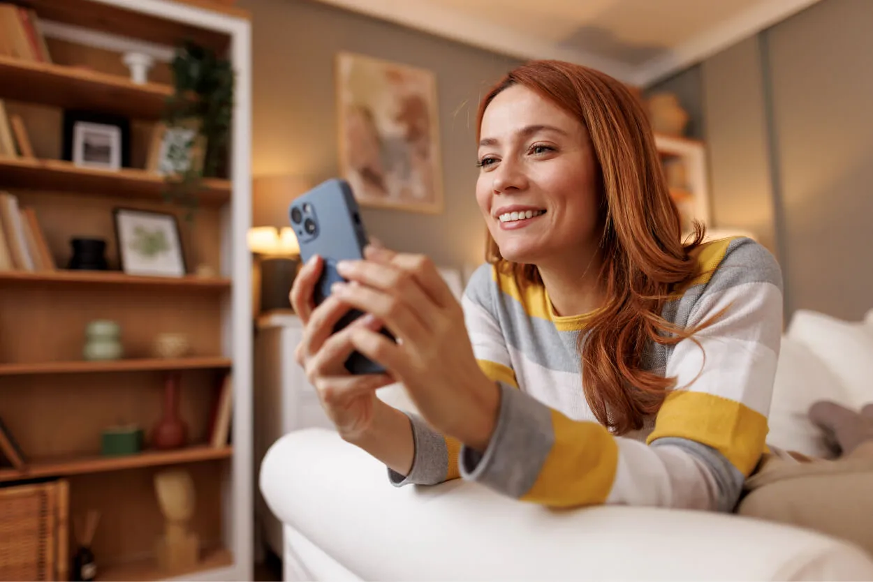 A woman on a sofa holding a phone and smiling