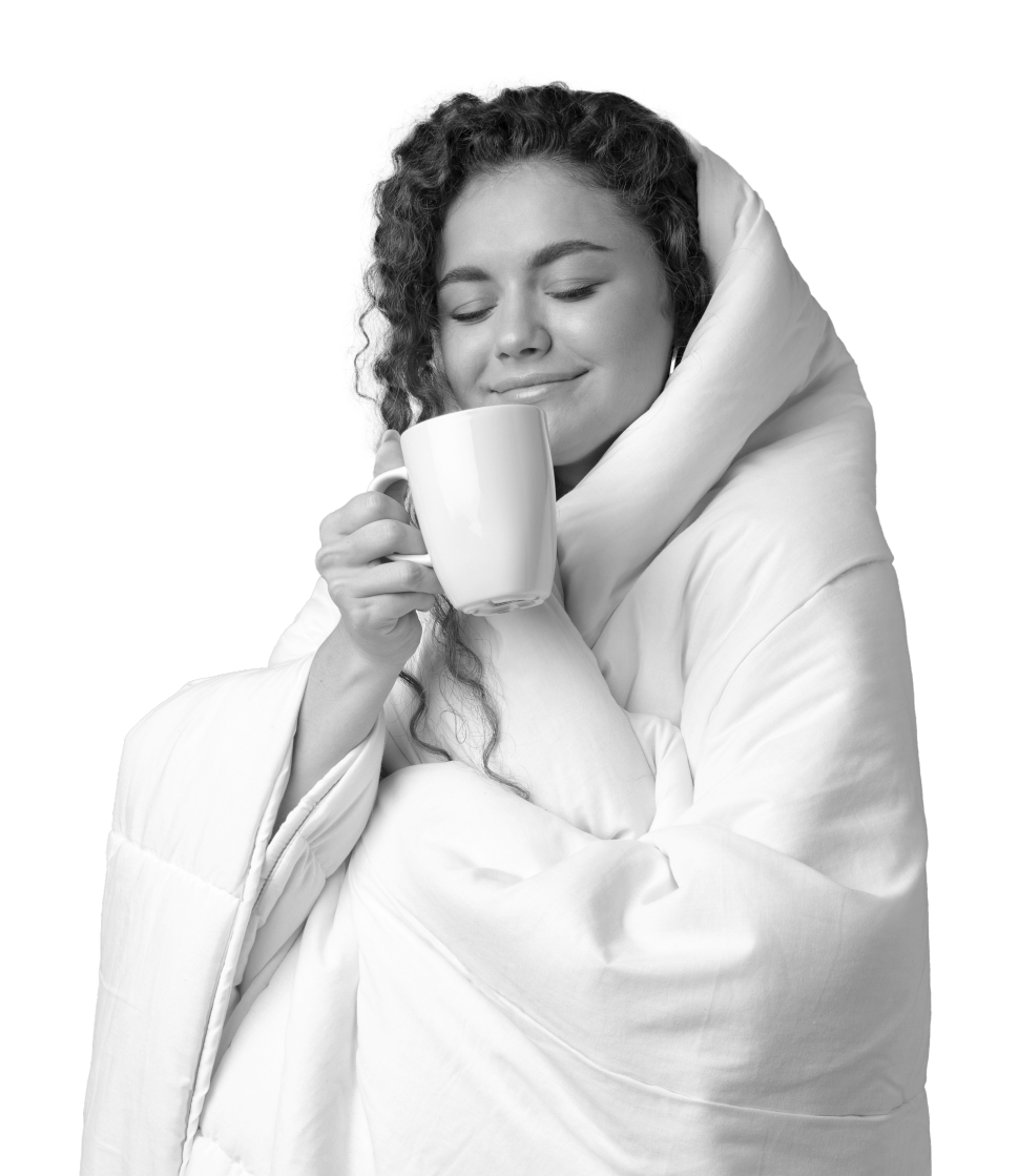 A woman wrapped up in her duvet smiling whilst holding a mug