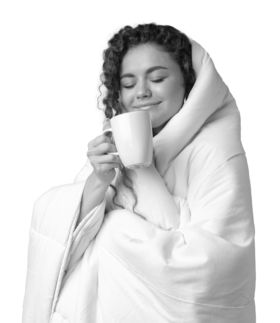 A woman wrapped up in her duvet smiling whilst holding a mug